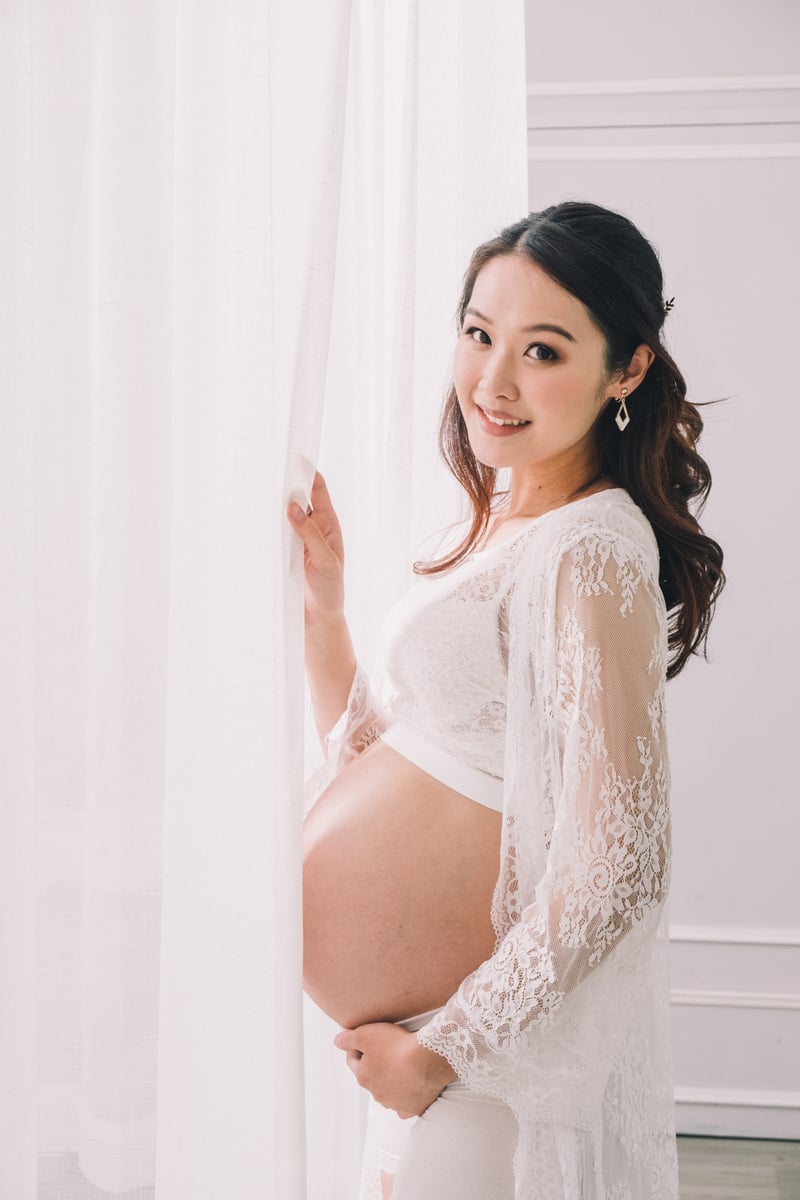 Asian pregnant woman standing near white curtain